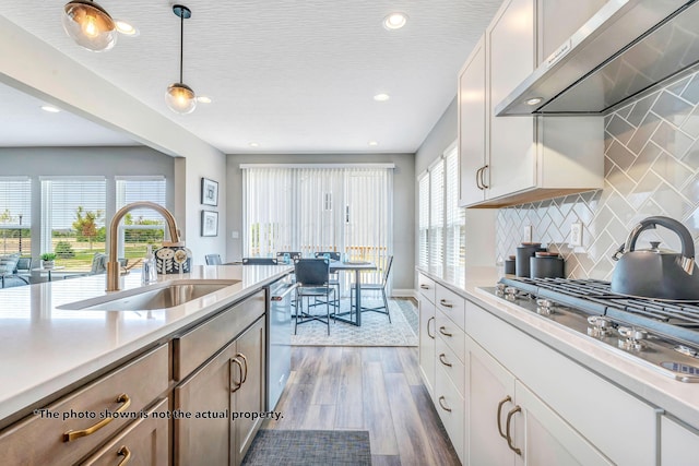 kitchen with sink, wall chimney exhaust hood, dark hardwood / wood-style floors, decorative light fixtures, and white cabinetry