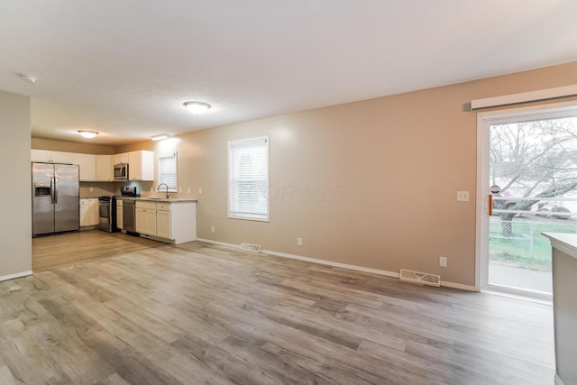 unfurnished living room featuring plenty of natural light, light wood-type flooring, and sink