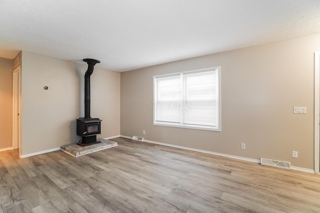 unfurnished living room featuring a wood stove and light hardwood / wood-style floors