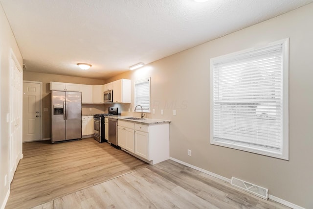 kitchen with appliances with stainless steel finishes, light wood-type flooring, white cabinetry, and sink