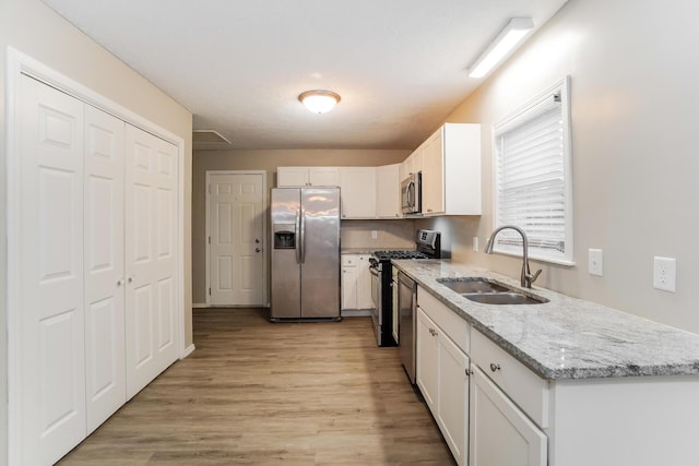 kitchen featuring appliances with stainless steel finishes, light wood-type flooring, light stone counters, sink, and white cabinetry