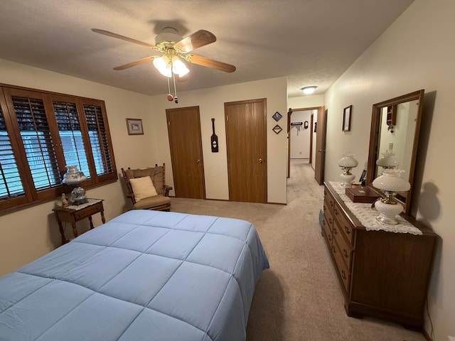 bedroom featuring multiple closets, ceiling fan, light colored carpet, and a textured ceiling