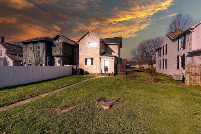 back house at dusk featuring a yard and central AC unit