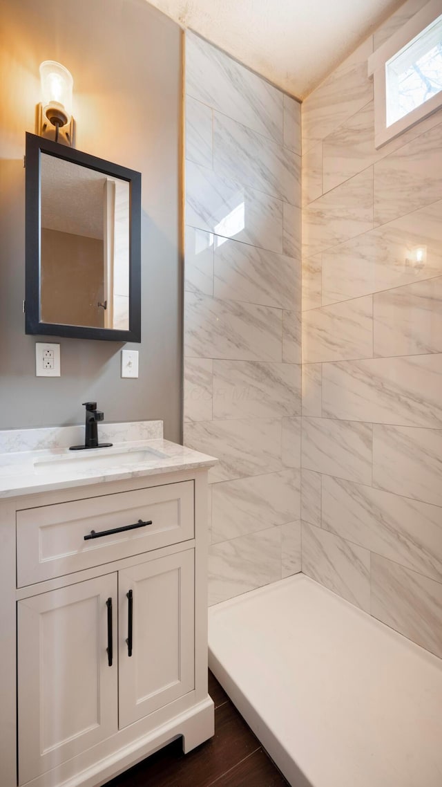 bathroom with hardwood / wood-style flooring, vanity, and tiled shower