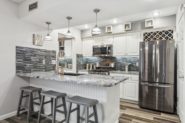 kitchen featuring kitchen peninsula, light stone counters, stainless steel appliances, white cabinets, and hanging light fixtures