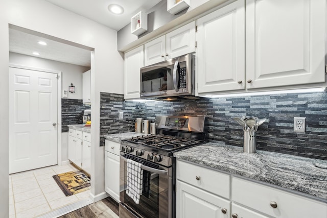 kitchen featuring light stone countertops, tasteful backsplash, stainless steel appliances, white cabinets, and light tile patterned flooring