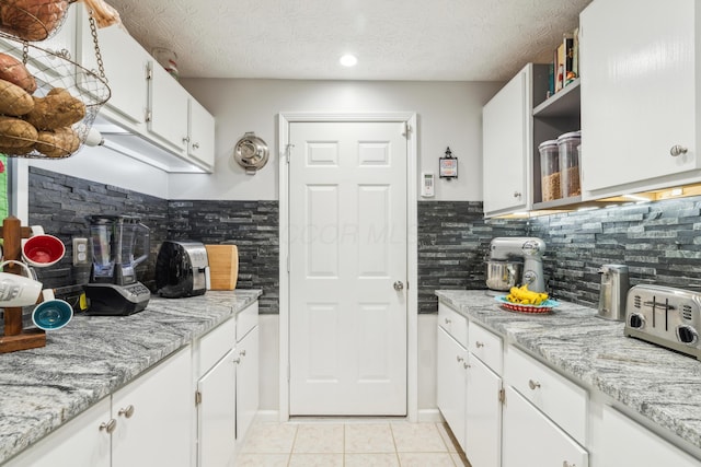 kitchen featuring backsplash, light stone countertops, and white cabinets