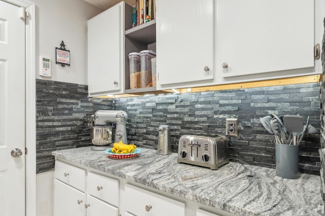 kitchen featuring decorative backsplash, light stone counters, and white cabinetry