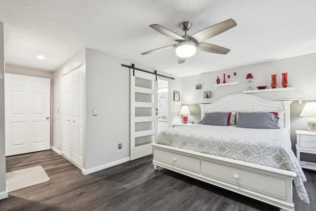 bedroom with a barn door, ceiling fan, a closet, and dark hardwood / wood-style flooring