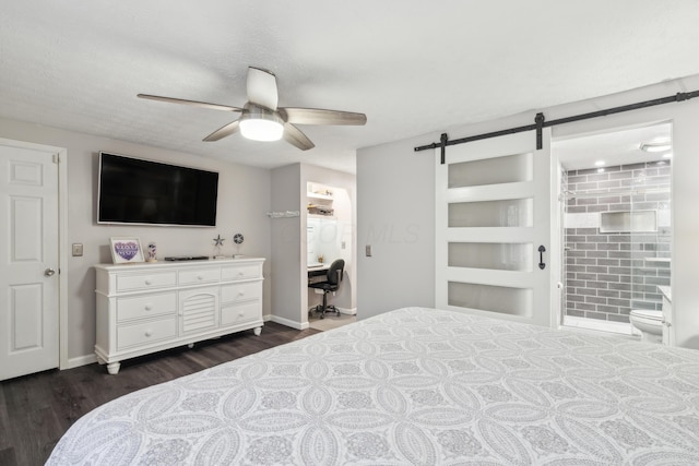 bedroom with ensuite bathroom, a barn door, dark wood-type flooring, and ceiling fan