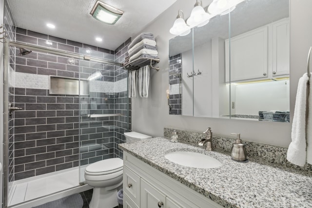 bathroom featuring vanity, toilet, a shower with shower door, and a textured ceiling