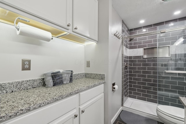 bathroom featuring toilet, vanity, a textured ceiling, and walk in shower