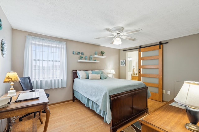 bedroom featuring light wood-type flooring, a textured ceiling, a barn door, and ceiling fan