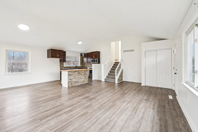 unfurnished living room featuring plenty of natural light, vaulted ceiling, and light wood-type flooring