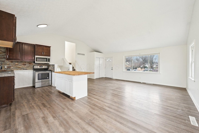 kitchen featuring butcher block counters, backsplash, vaulted ceiling, stainless steel range with electric cooktop, and hardwood / wood-style flooring