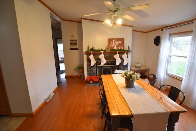 dining space featuring crown molding, ceiling fan, a fireplace, and wood-type flooring