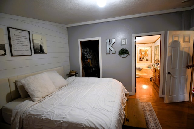 bedroom featuring a walk in closet, ensuite bathroom, a textured ceiling, dark wood-type flooring, and a closet