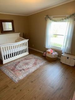 unfurnished bedroom with wood-type flooring, a nursery area, and ornamental molding