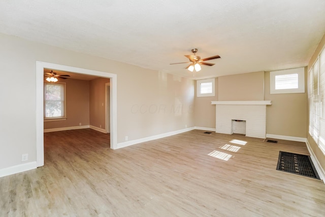 unfurnished living room with a textured ceiling, light wood-type flooring, a brick fireplace, and ceiling fan