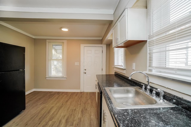 kitchen featuring white cabinets, black fridge, sink, light hardwood / wood-style flooring, and ornamental molding