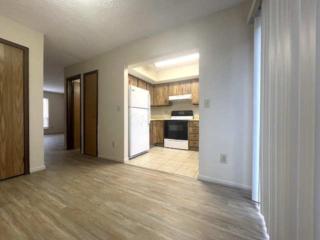 kitchen featuring light hardwood / wood-style floors, white appliances, a textured ceiling, and a tray ceiling