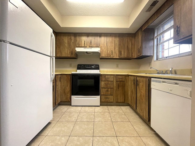 kitchen featuring a tray ceiling, sink, light tile patterned floors, and white appliances