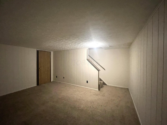 basement featuring carpet flooring, a textured ceiling, and wooden walls