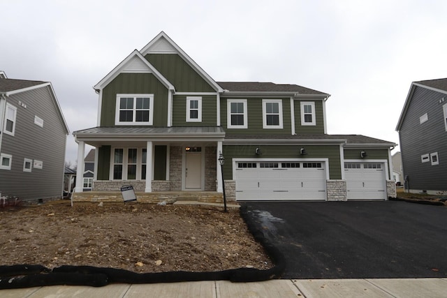 craftsman-style house featuring a standing seam roof, aphalt driveway, stone siding, covered porch, and board and batten siding