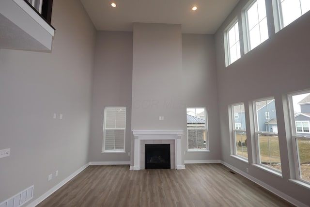 unfurnished living room featuring wood finished floors, visible vents, baseboards, a fireplace, and a towering ceiling