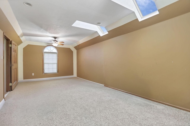 interior space featuring vaulted ceiling with skylight, ceiling fan, and light carpet