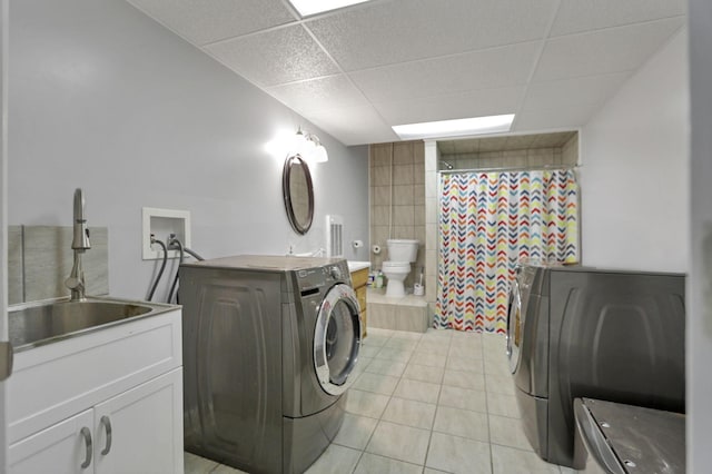 clothes washing area featuring washer and dryer, light tile patterned floors, tile walls, and sink