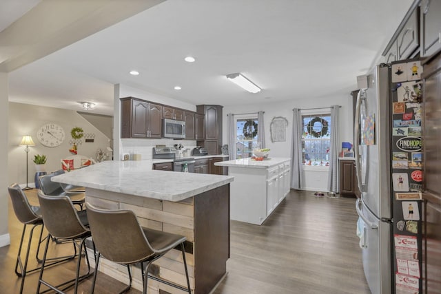 kitchen with hardwood / wood-style floors, a kitchen breakfast bar, dark brown cabinets, kitchen peninsula, and stainless steel appliances