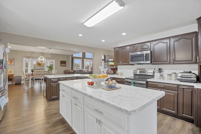 kitchen with appliances with stainless steel finishes, light wood-type flooring, tasteful backsplash, white cabinets, and a kitchen island