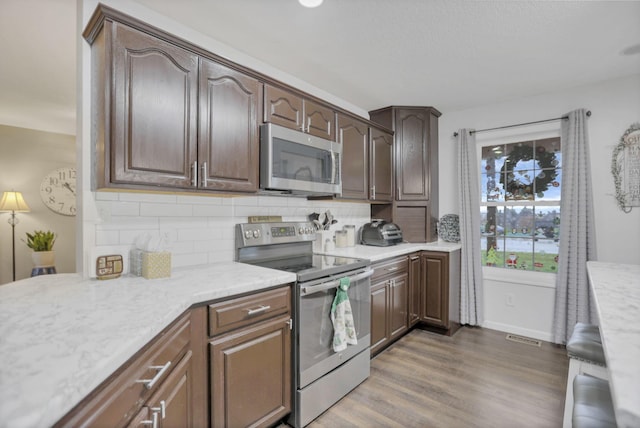 kitchen with hardwood / wood-style flooring, appliances with stainless steel finishes, dark brown cabinets, and tasteful backsplash