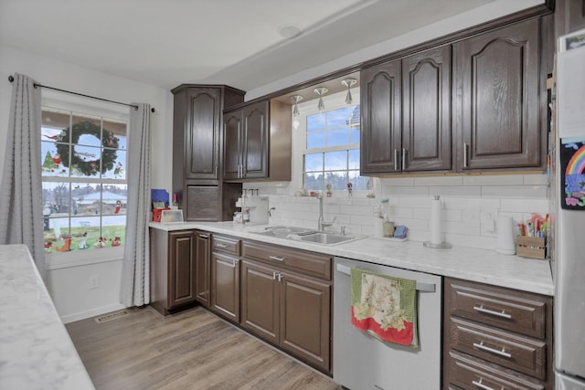 kitchen with sink, stainless steel dishwasher, decorative backsplash, dark brown cabinets, and light hardwood / wood-style floors