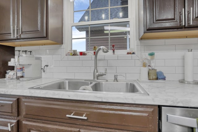 kitchen featuring backsplash, dark brown cabinetry, light stone countertops, and sink