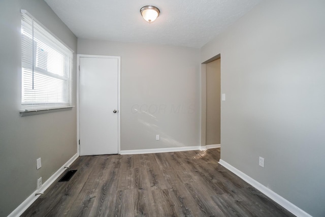 unfurnished room featuring dark wood-type flooring and a textured ceiling