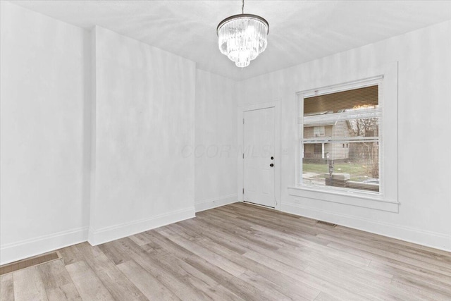 spare room featuring a chandelier and light hardwood / wood-style flooring