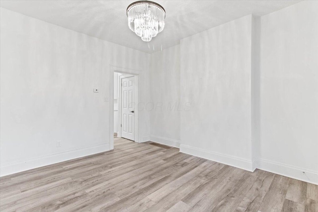 empty room with light hardwood / wood-style flooring and a chandelier