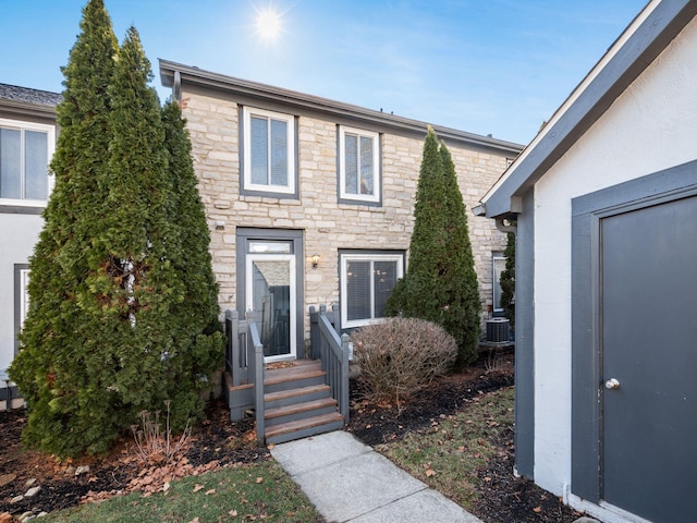 view of front of property with stone siding, central AC, and stucco siding