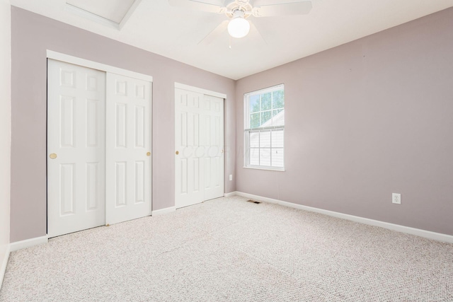 unfurnished bedroom featuring carpet flooring, ceiling fan, and two closets