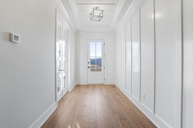 doorway to outside with light wood-type flooring, a raised ceiling, crown molding, and baseboards