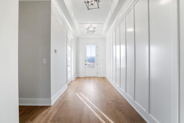 hallway featuring ornamental molding, light wood-type flooring, visible vents, and baseboards