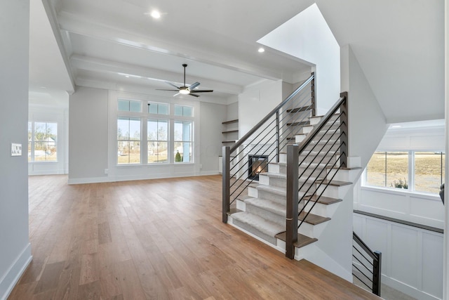 stairway featuring ceiling fan, wood finished floors, beam ceiling, and a healthy amount of sunlight