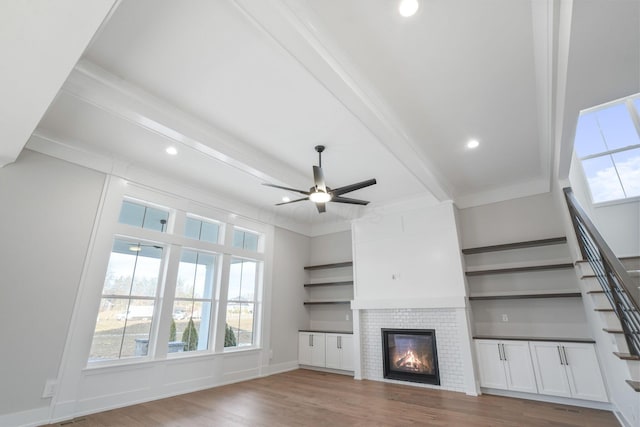 unfurnished living room featuring a tile fireplace, ceiling fan, wood finished floors, beamed ceiling, and stairs