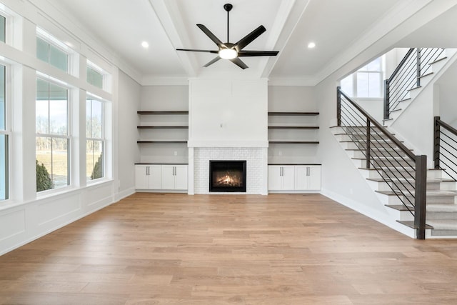 unfurnished living room featuring crown molding, stairway, a large fireplace, light wood-type flooring, and beamed ceiling