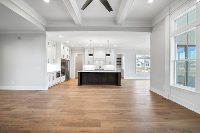 kitchen featuring white cabinets, light countertops, beamed ceiling, a center island with sink, and pendant lighting