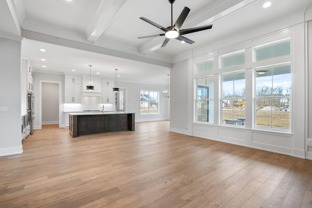 unfurnished living room featuring beam ceiling, ornamental molding, light wood-type flooring, baseboards, and ceiling fan with notable chandelier