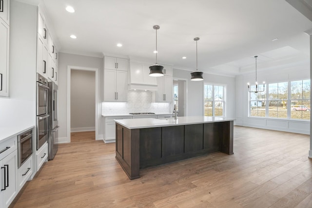 kitchen with decorative light fixtures, a center island with sink, gas stovetop, light countertops, and white cabinets