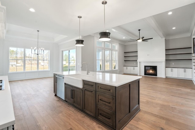 kitchen with open floor plan, light countertops, stainless steel dishwasher, pendant lighting, and a sink